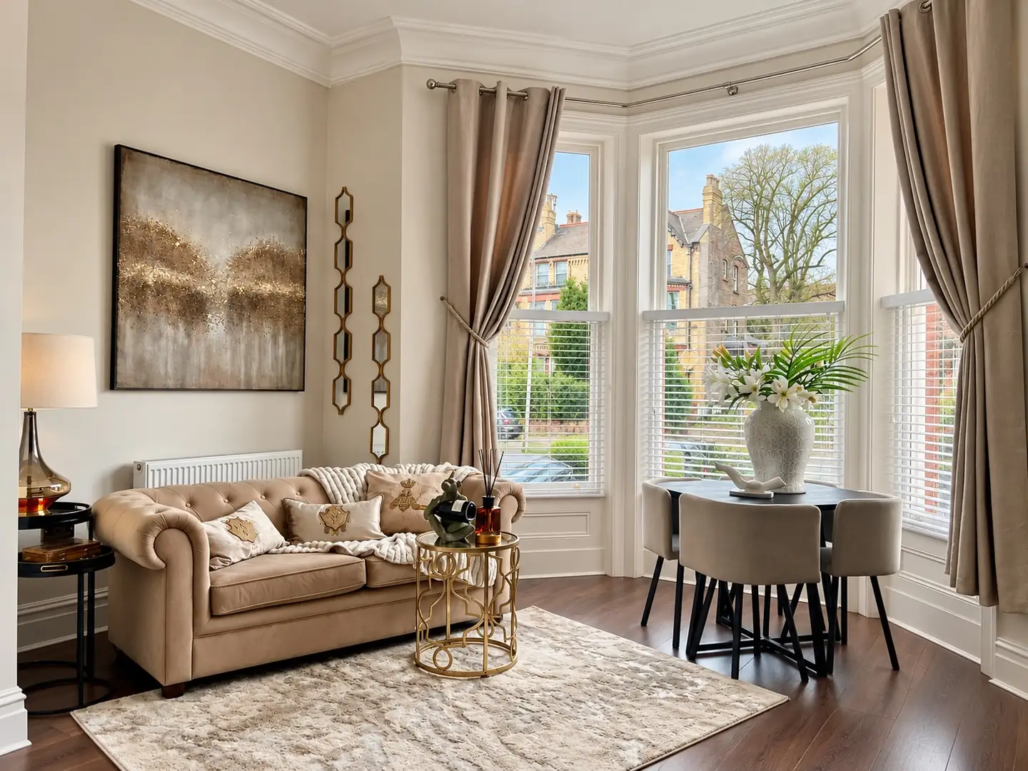 Bay window lounge with a chesterfield sofa, gold side table, dining set and abstract artwork