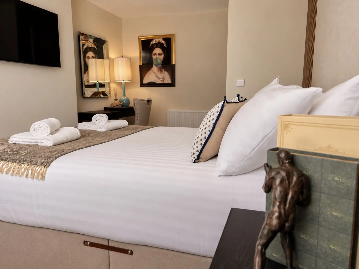 Bedroom with striped bedding, rolled towels and a bubblegum portrait on the wall