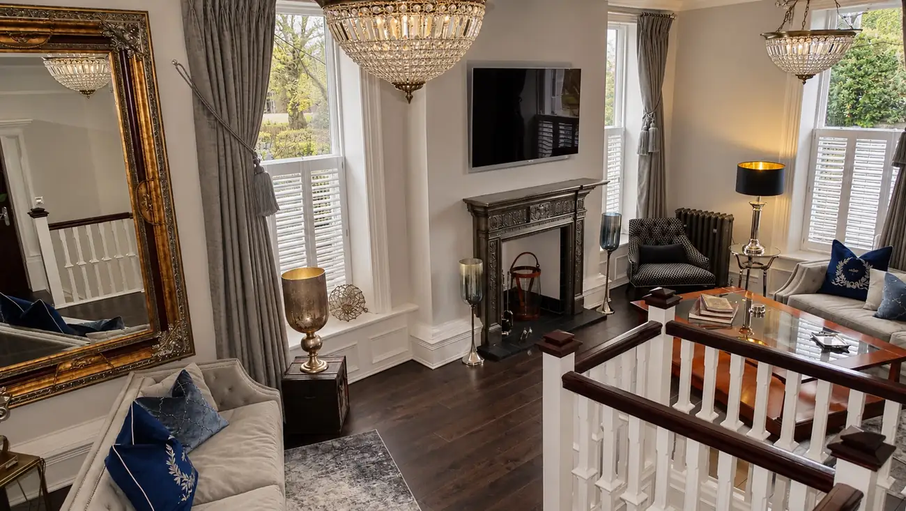 After: the finished living room with a cast iron fireplace, chandelier, shutters and a patterned armchair