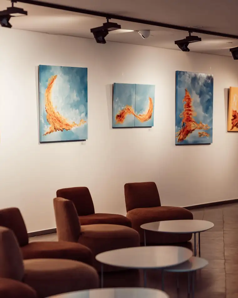 Three paintings hung above lounge chairs in the gallery