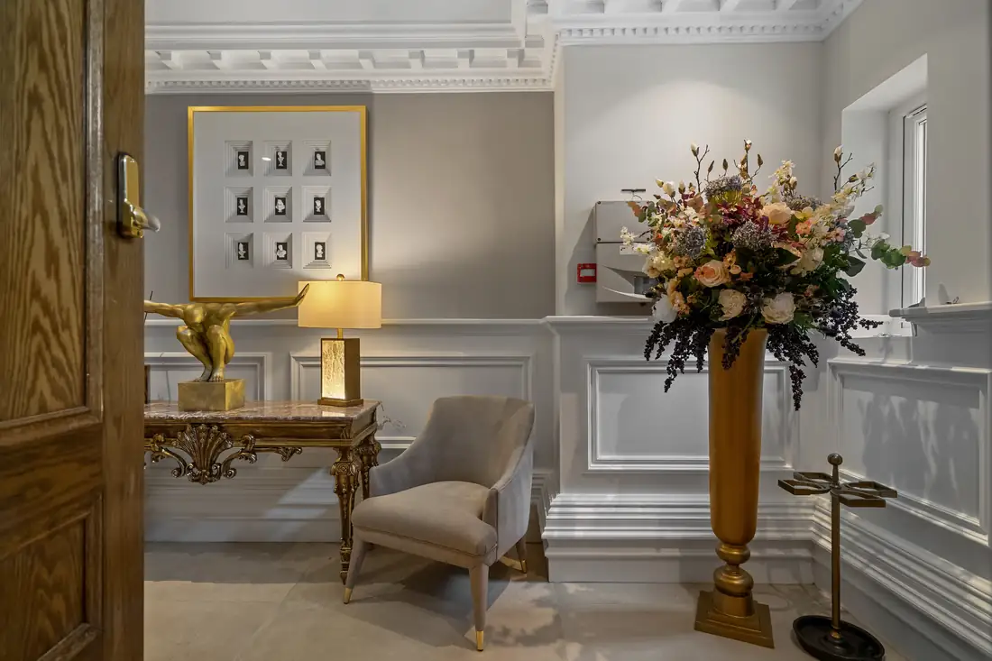 Entrance hall console with a gilt lamp, armchair and tall floral arrangement